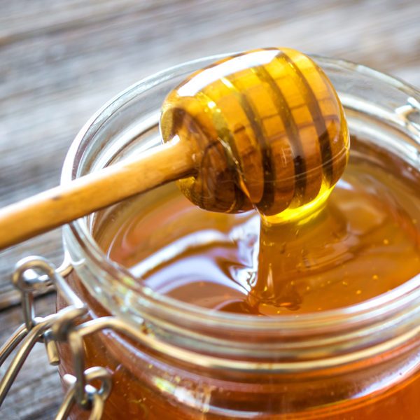 Honey dripping from a wooden dipper into a jar